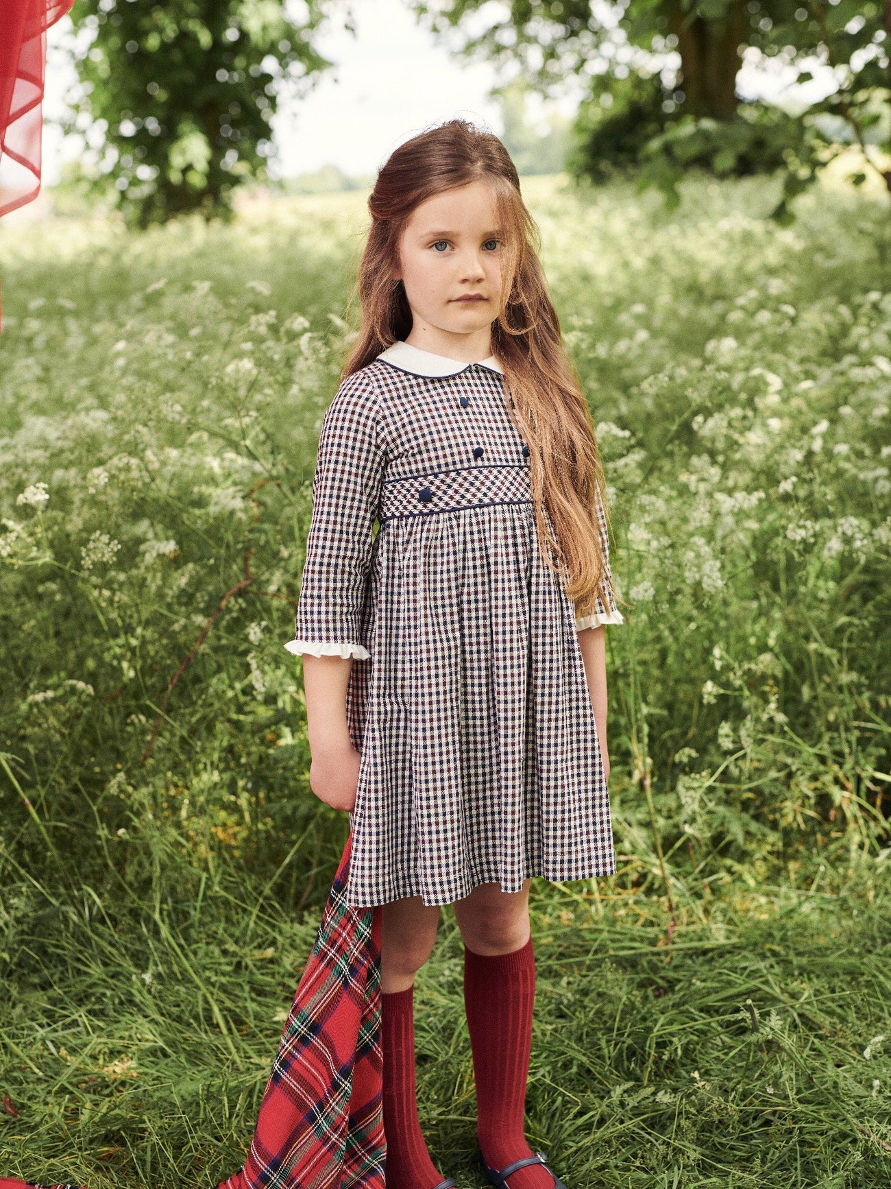 A young girl modeling a stylish navy and white checkered dress with a Peter Pan collar, paired with maroon knee-high socks.